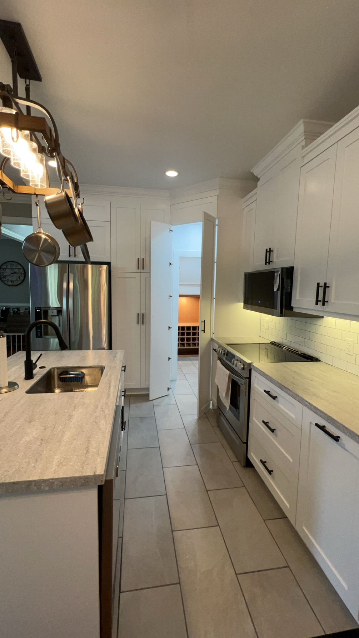 Completed white kitchen with pot rack, pantry door, and wine storage